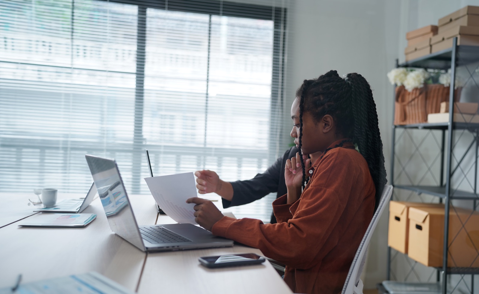 Two colleagues checking paperwork against a laptop screen